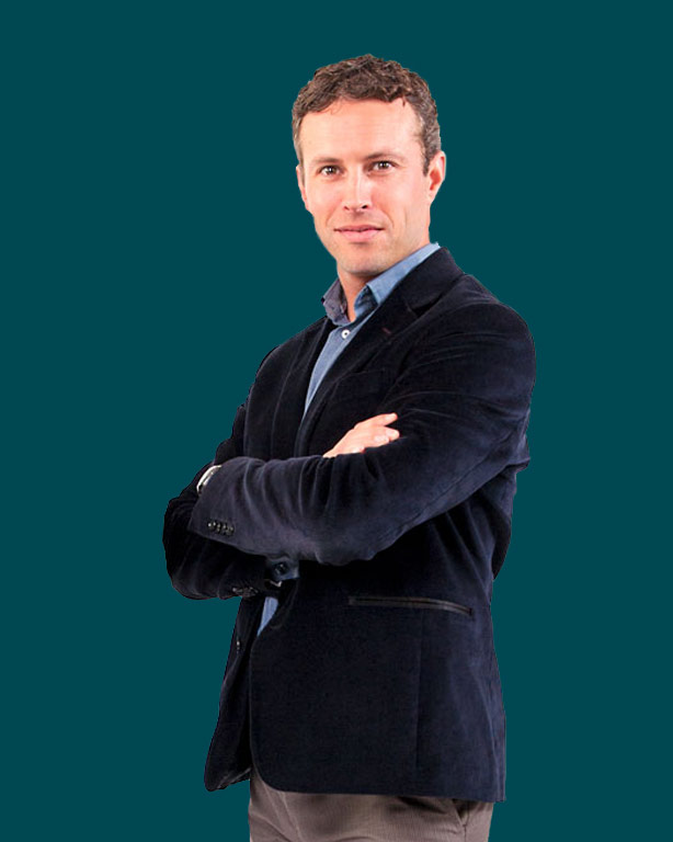 A guy in suede suit and denim shirts and brown suit pants crossing arms with dark green background
