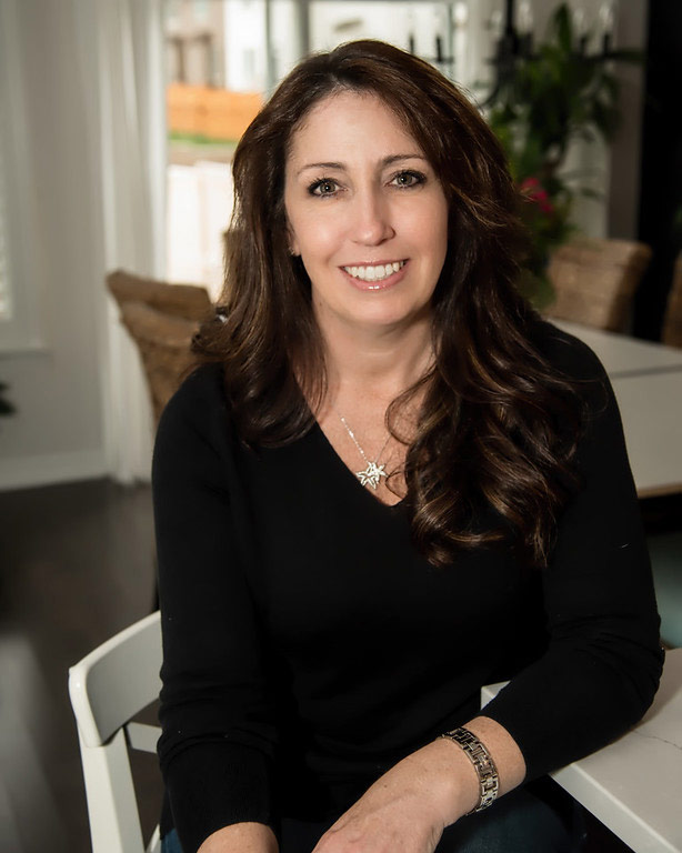 Smiling young professional woman in long dark hair and black v neck top sitting on the chair